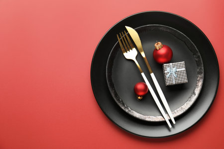 Christmas setting with plates, cutlery and festive decor on red background, top view. Space for text