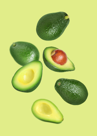 Fresh avocado falling on light green background. Whole and sliced