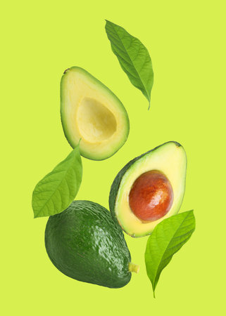 Fresh avocado and leaves falling on light green background