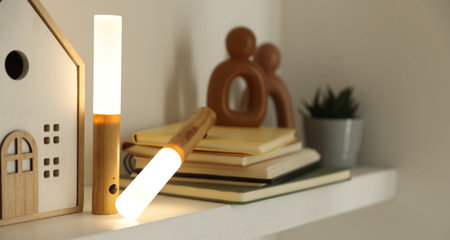 Portable LED lamps, books and decor on white shelf, closeup
