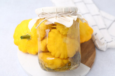 Pickled pattypan squashes in glass jar and fresh vegetables on white table, closeupの写真素材