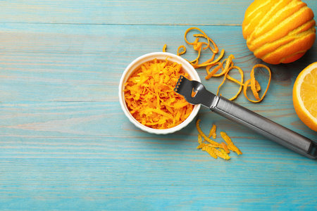 Orange zest, fresh fruits and zester tool on light blue wooden table, flat lay. Space for text