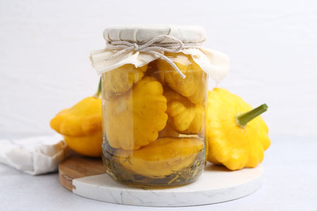 Pickled pattypan squashes in glass jar and fresh vegetables on white table, closeupの写真素材