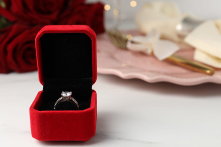 Romantic dinner. Box with engagement ring on white table, closeup. Space for text