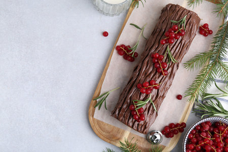 Delicious Yule log (traditional Christmas cake) with redcurrant and fir tree branches on light table, flat lay. Space for textの写真素材