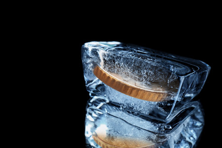 Golden coin in ice cube on black background.の写真素材