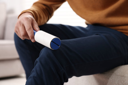 Man cleaning pants with lint roller on pouf at home, closeupの写真素材