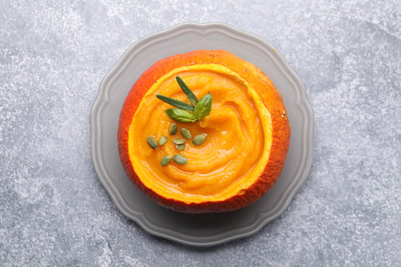 Tasty pumpkin cream soup with seeds and basil served in pumpkin on gray table, top viewの写真素材