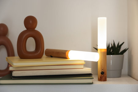 Portable LED lamps, books and decor on white shelf, closeup