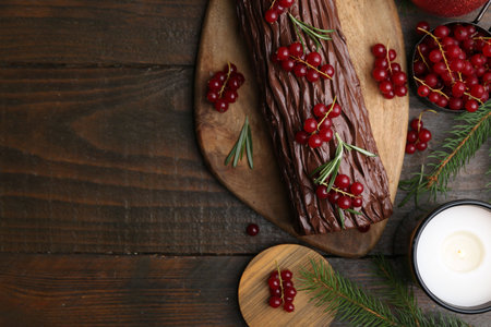 Delicious Yule log (traditional Christmas cake) with redcurrant, candle and fir tree branches on wooden table, flat lay. Space for textの写真素材