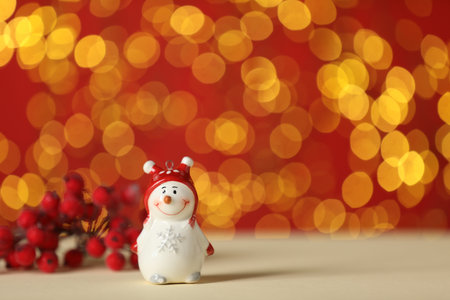 Cute decorative snowman on beige table against red background with blurred lights, closeup. Space for textの写真素材