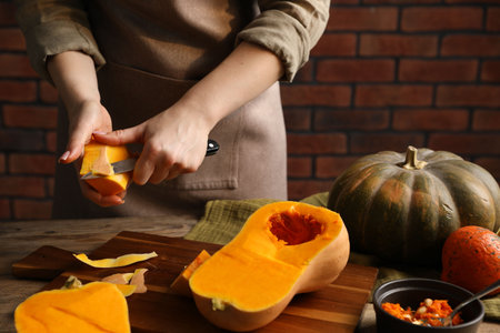 Woman peeling pumpkin at wooden table against brick wall, closeupの写真素材