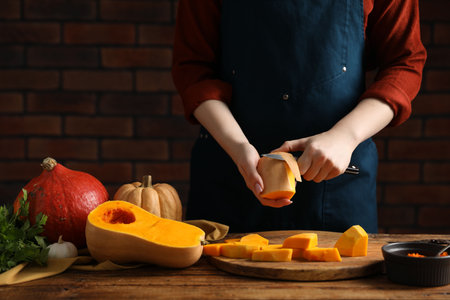 Woman peeling pumpkin at wooden table against brick wall, closeupの写真素材
