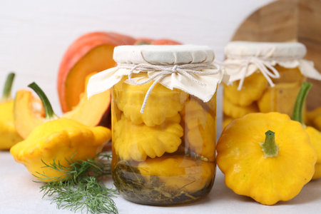 Pickled pattypan squashes in jars, fresh vegetables and dill on light table, closeupの写真素材