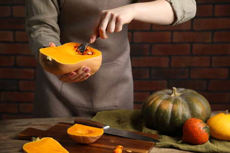 Woman removing pumpkin seeds at wooden table against brick wall, closeupの写真素材