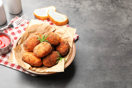 Delicious patties with rosemary in bowl, bread and ketchup on gray textured table. Space for text