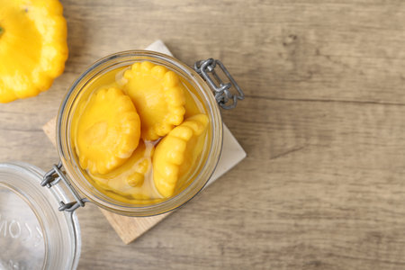 Pickled pattypan squashes in glass jar on wooden table, top view. Space for textの写真素材