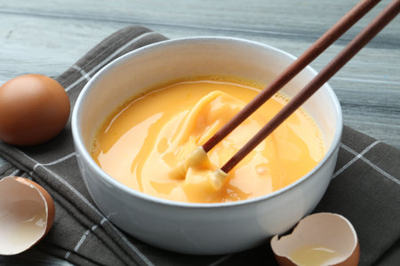 Beaten eggs in bowl and chopsticks on table, closeupの写真素材