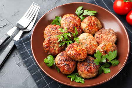 Delicious patties with parsley in bowl on gray textured table, closeup