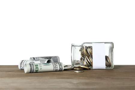 Overturned jar with blank note and money on wooden table against white background