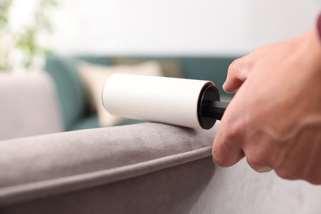 Man cleaning sofa with lint roller at home, closeupの写真素材