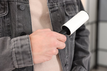 Man cleaning denim jacket with lint roller at home, closeupの写真素材