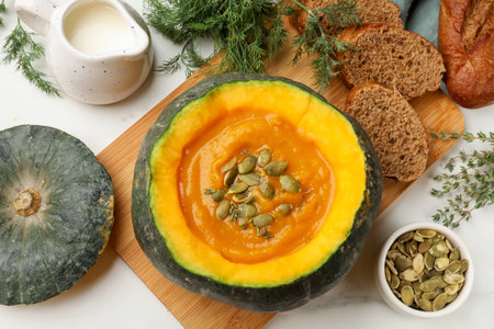 Tasty pumpkin cream soup with seeds and thyme served in pumpkin on light table, flat layの写真素材
