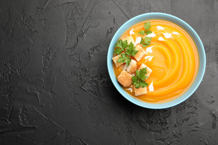 Tasty pumpkin cream soup with parsley and croutons in bowl on dark textured table, top view. Space for textの写真素材