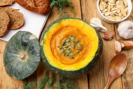 Tasty pumpkin cream soup with seeds and thyme served in pumpkin on wooden table, flat layの写真素材