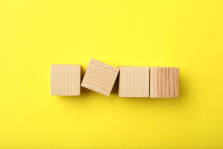 Wooden cubes on yellow background, top view