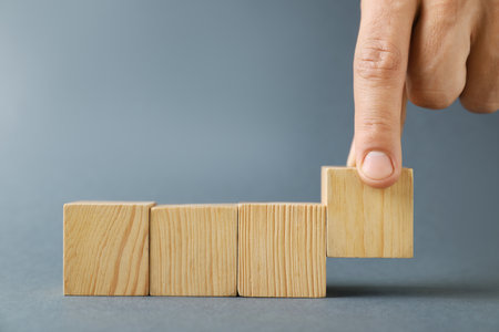 Man with wooden cubes on gray background, closeup. Space for textの写真素材