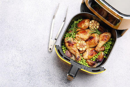 Air fryer with grilled chicken drumsticks, spices, green peas and tongs on gray table, top view. Space for textの写真素材