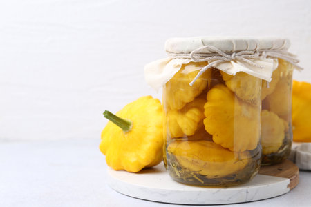 Pickled pattypan squashes in jars and fresh vegetables on white table, closeup. Space for textの写真素材