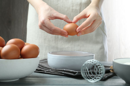 Woman breaking egg at table indoors, closeupの写真素材