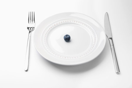 One blueberry on plate and cutlery on white table, closeupの写真素材