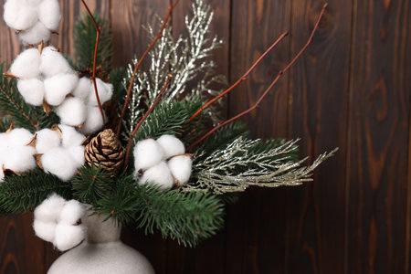 Beautiful composition with cotton, pine tree branches in vase near wooden wall indoors, closeup. Winter decorの写真素材