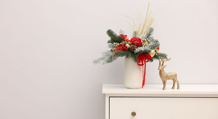 Beautiful composition with fir tree branches in vase and reindeer figure on white chest of drawers near light wall indoors, space for text. Winter decorの写真素材