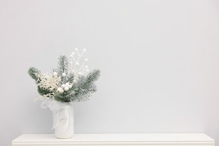 Beautiful composition with fir tree branches in vase on shelf near white wall indoors, space for text. Winter decorの写真素材