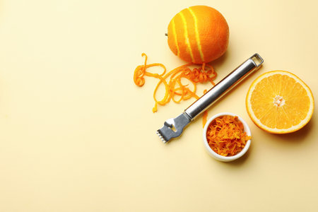 Orange zest, fresh fruits and zester tool on beige background, flat lay. Space for textの写真素材