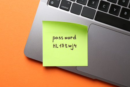Paper note with password and laptop on orange background, top viewの写真素材