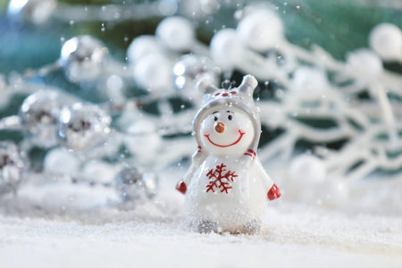 Cute decorative snowman on artificial snow against blurred background, closeup