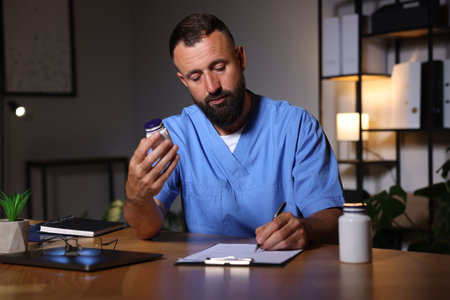 Tired doctor writing notes at table in clinic during night shiftの写真素材