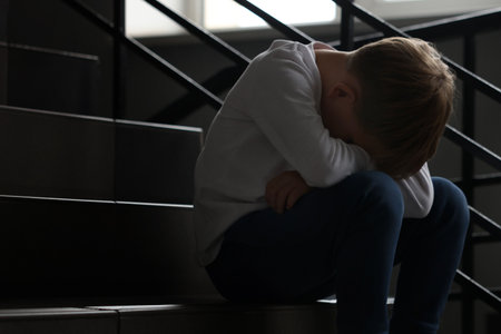 Upset little boy on stairs indoors, space for textの写真素材