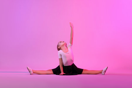 Little girl doing gymnastic exercise on violet background in color lightの写真素材
