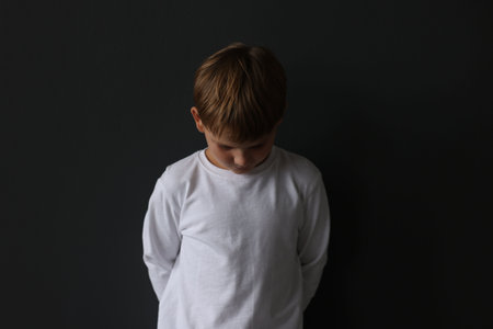 Upset little boy standing on black backgroundの写真素材