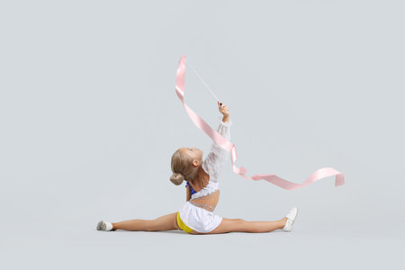 Little girl doing gymnastic exercise with ribbon on gray backgroundの写真素材