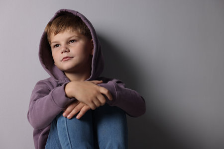 Upset little boy near light gray wall indoors, space for textの写真素材