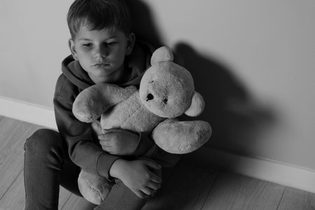 Upset little boy with toy bear indoors, above view. Black and white effectの写真素材