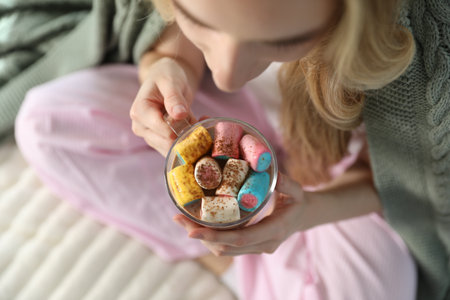 Beautiful woman wrapped in plaid having tasty hot cocoa with marshmallows on bed at home, above viewの写真素材
