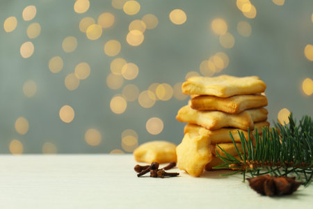Cookies in shape of stars, spices and fir tree branches on light wooden table against gray background with blurred lights, closeup with space for text. Merry Christmasの写真素材